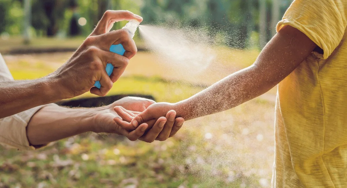 Person spraying mosquito repellent on a child’s arm outdoors
