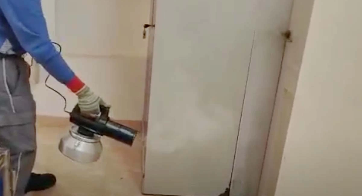 Technician using a sprayer to apply pest control treatment indoors